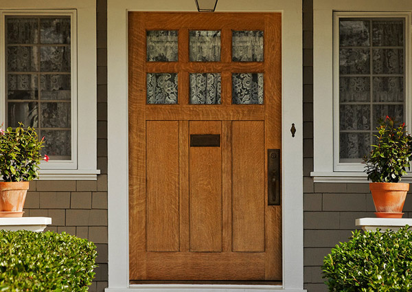 Wooden front door with side windows and plants.